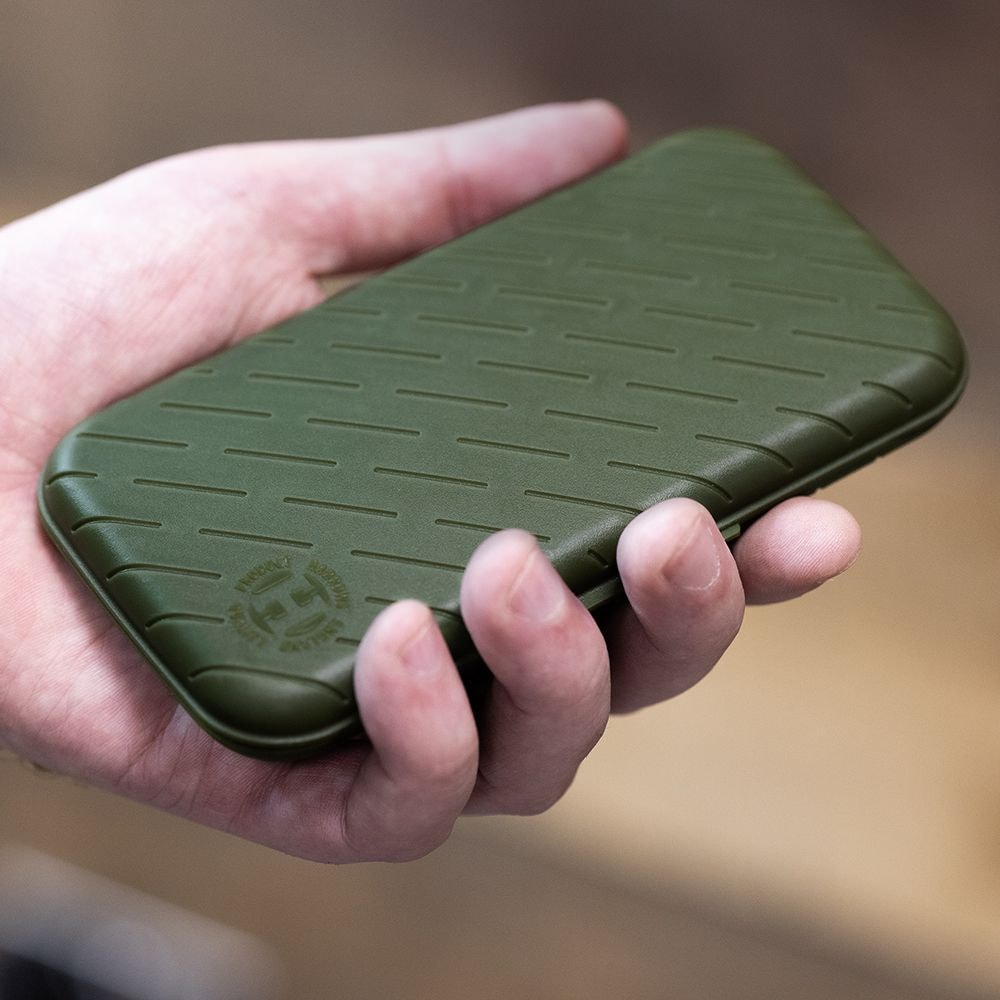 Etui na lotki Harrows Slimcase Eine Hand hält ein schlankes, grünes Etui. Das Etui hat ein strukturiertes Muster und ein rundes Logo in der Ecke.