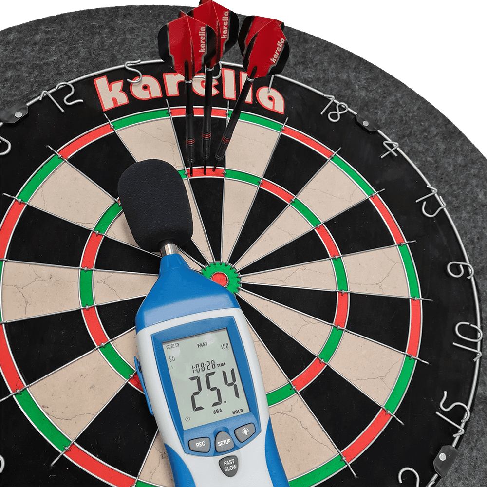 811501_Karella_Schallschutz_f-r_Steeldartboards_40AsdKuqQ3Dv9I Das Bild zeigt ein Steeldartboard mit integriertem Schallschutz und Auffangring von Karella. Auf dem Dartboard liegen drei rote Darts sowie ein Schallpegelmessgerät, das 25,4 dB anzeigt.