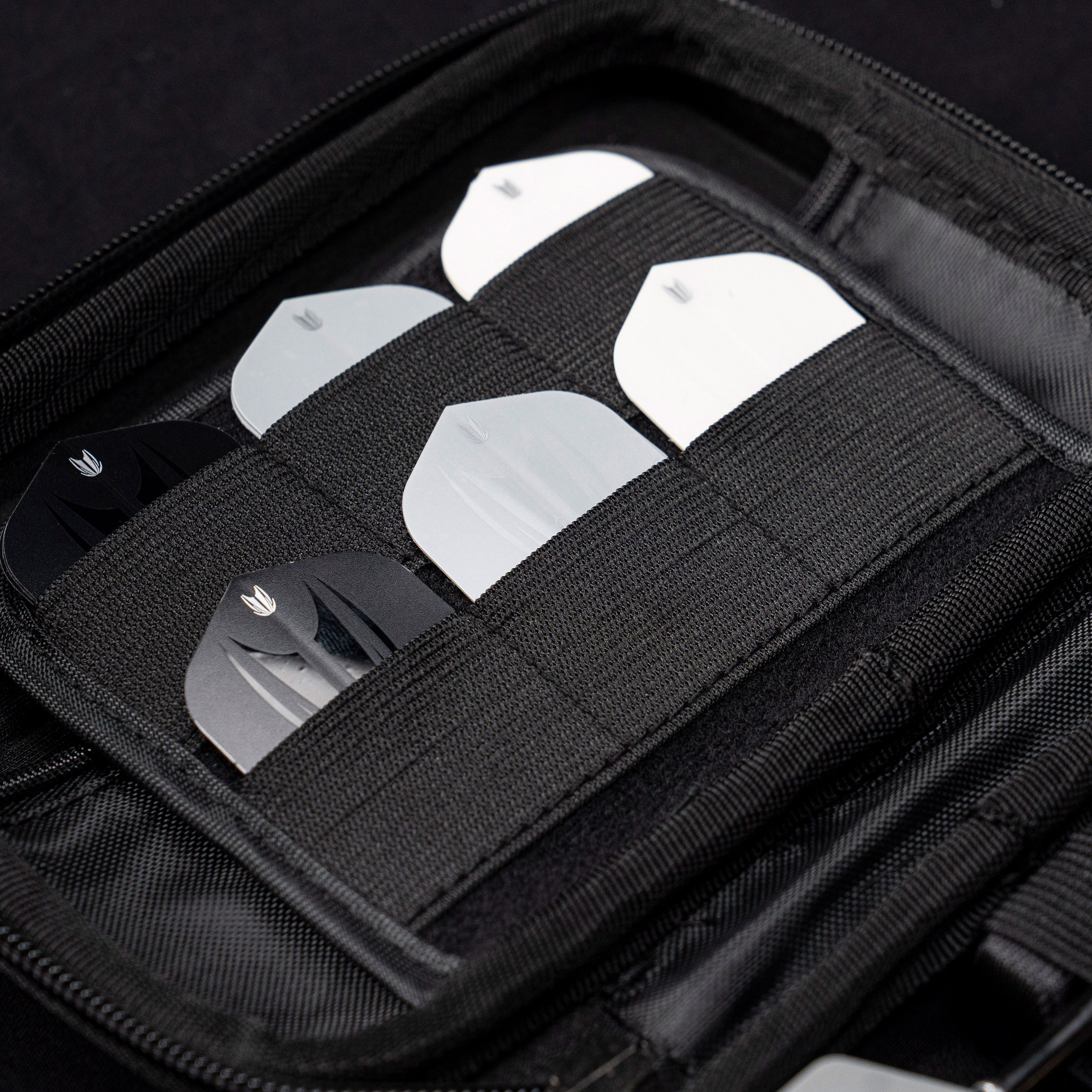 Pokrowiec na rzutki Takoma Ghost Series Raymond Van Barneveld Das Bild zeigt das Target Takoma Bolide Dartcase, in dem mehrere Dart-Flights ordentlich in elastischen Halterungen verstaut sind. Das Case ist schwarz und bietet sicheren Schutz für das Dartzubehör.