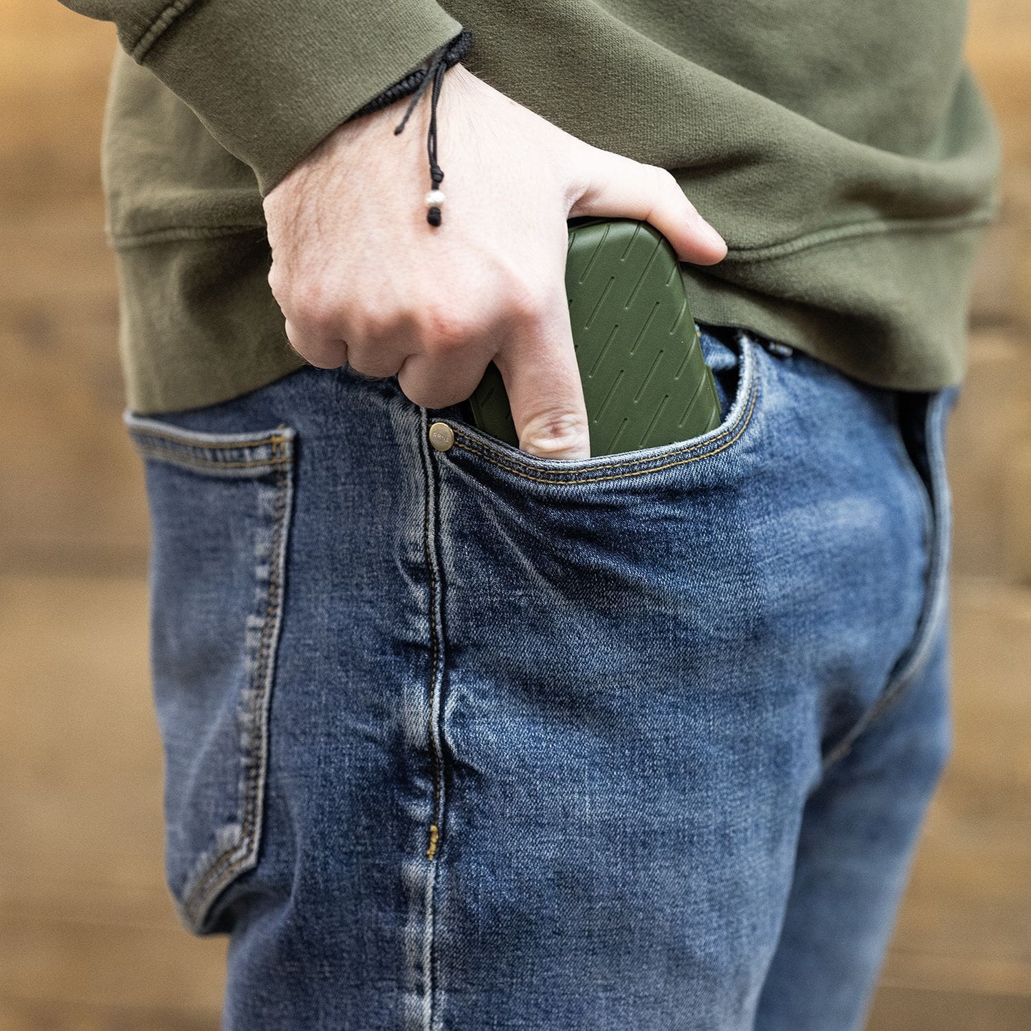 Etui na lotki Harrows Slimcase Eine Person steckt ein grünes Etui in die vordere Hosentasche einer Jeans. Das Etui hat eine strukturierte Oberfläche und passt gut in die Tasche.