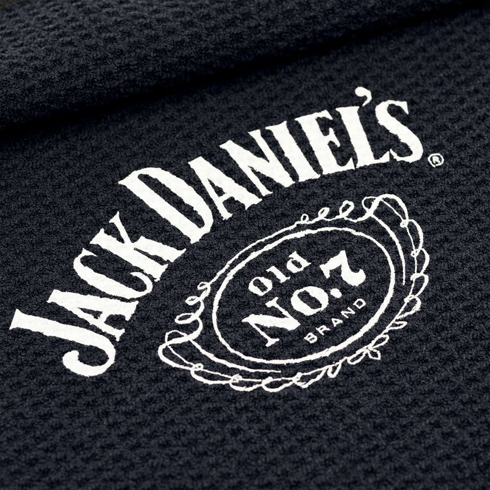 JD7032_Mission_Jack_Daniels_Handtuch_2 Das Bild zeigt ein schwarzes Handtuch mit dem weißen Jack Daniel's Logo darauf. Das bekannte "Old No. 7 Brand"-Design ist in der Mitte gut sichtbar.