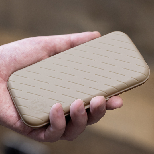 Etui na lotki Harrows Slimcase Eine Hand hält ein schlankes, steingraues Etui mit einem dezenten Muster. Das Etui wirkt stabil und ist wahrscheinlich für Dartzubehör gedacht.