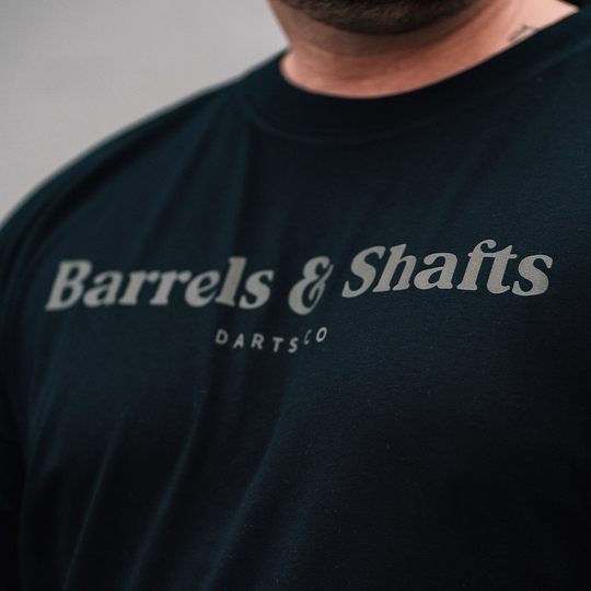 T-shirt „Barrels and Shafts” – czarny Das Bild zeigt ein schwarzes T-Shirt mit der Aufschrift "Barrels & Shafts". Darunter steht in kleineren Buchstaben "DARTSCO".