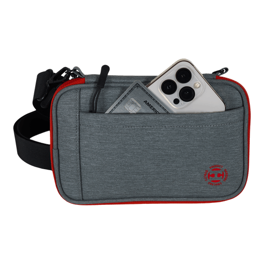 Etui na lotki Harrows Smart Case XL Das Bild zeigt eine graue Tasche mit rotem Rand und einem schwarzen Gurt. In der Vordertasche stecken ein Smartphone und eine Kreditkarte.