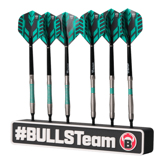 Das Bild zeigt sechs schwarze Dartpfeile mit grünen Akzenten, die ordentlich in einer Halterung stehen. Auf der Halterung steht groß "#BULLSTeam" und das Bulls-Logo ist sichtbar.