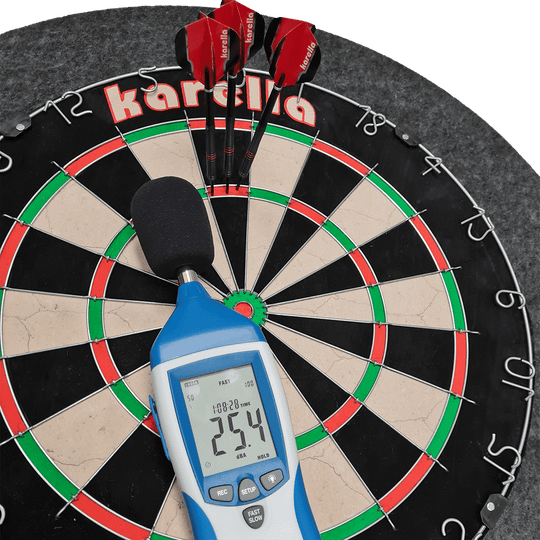 811501_Karella_Schallschutz_f-r_Steeldartboards_40AsdKuqQ3Dv9I Das Bild zeigt ein Steeldartboard mit integriertem Schallschutz und Auffangring von Karella. Auf dem Dartboard liegen drei rote Darts sowie ein Schallpegelmessgerät, das 25,4 dB anzeigt.