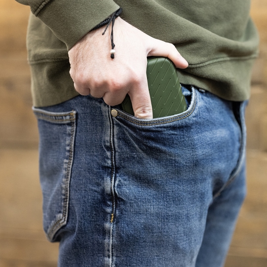 Etui na lotki Harrows Slimcase Eine Person steckt ein grünes Etui in die vordere Hosentasche einer Jeans. Das Etui hat eine strukturierte Oberfläche und passt gut in die Tasche.